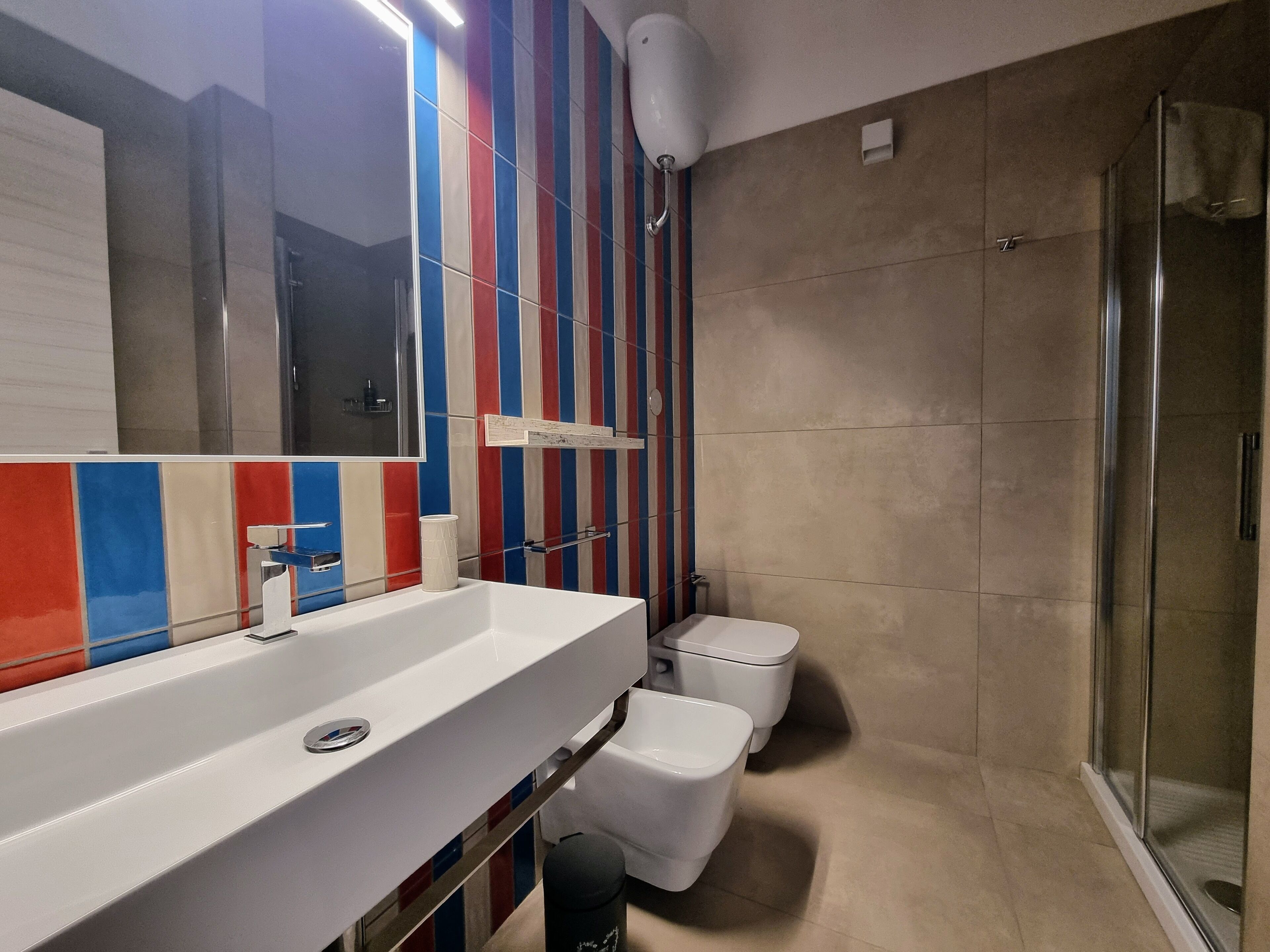 A modern bathroom with a large mirror, a white sink, a toilet, and a shower area.
