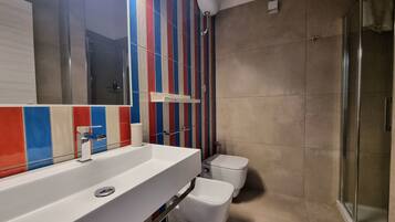 A modern bathroom with a large mirror, a white sink, a toilet, and a shower area.