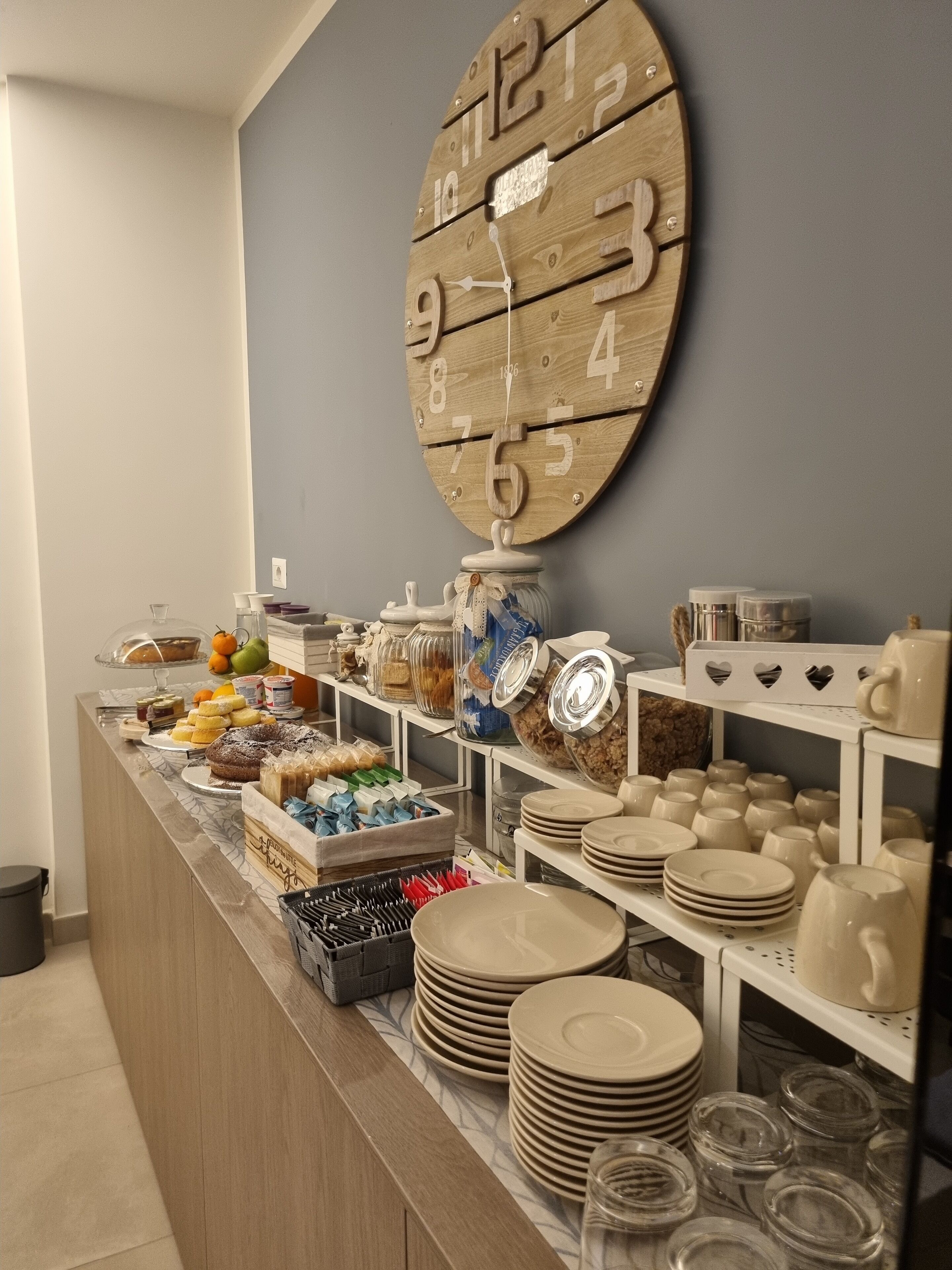 A buffet area with a wooden clock, various food items, and stacked plates and bowls.