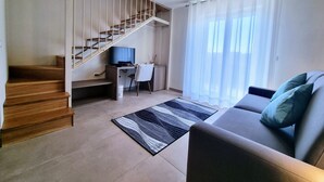 A living room with a sofa, a TV on a desk, a staircase, and a window with curtains. - Ro agrimaison  (Volla)