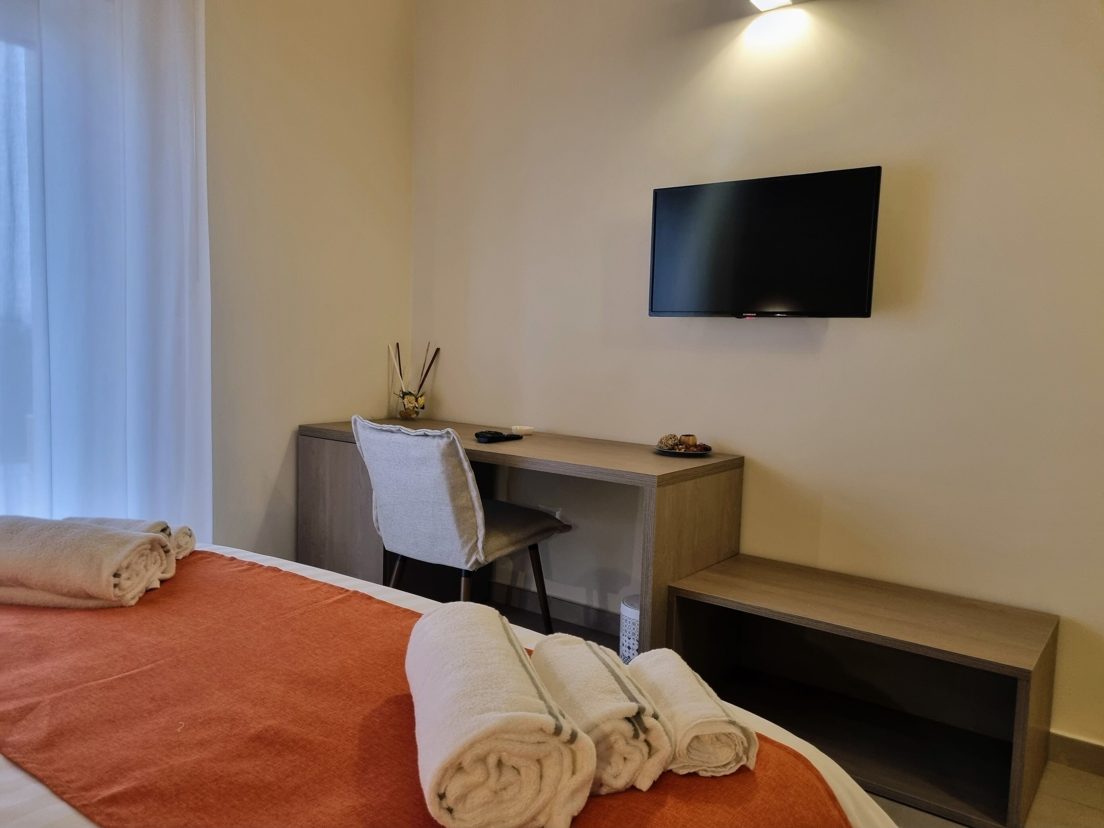 Habitación de hotel con cama, escritorio, silla, televisor y mesita de noche.