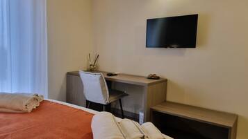 Habitación de hotel con cama, escritorio, silla, televisor y mesita de noche.