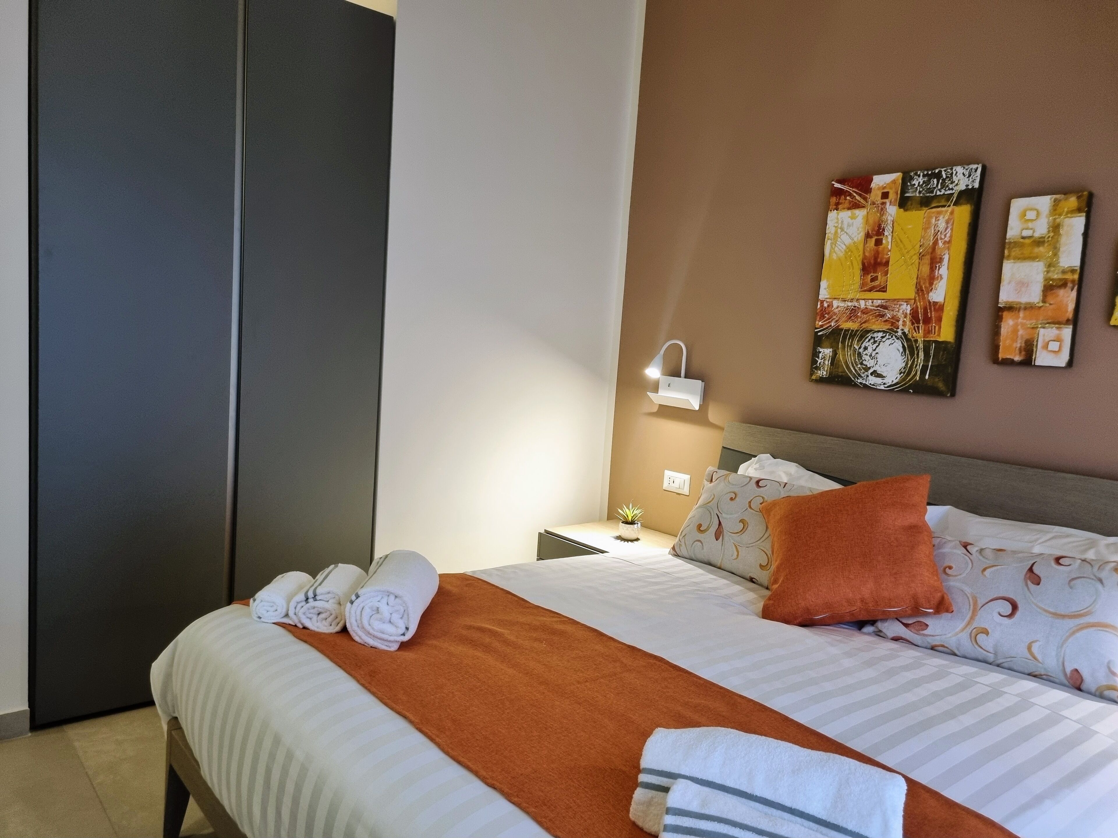 Ein ordentlich gemachtes Bett mit aufgerollten Handtüchern, einer braunen Tagesdecke und gemusterten Kissen.