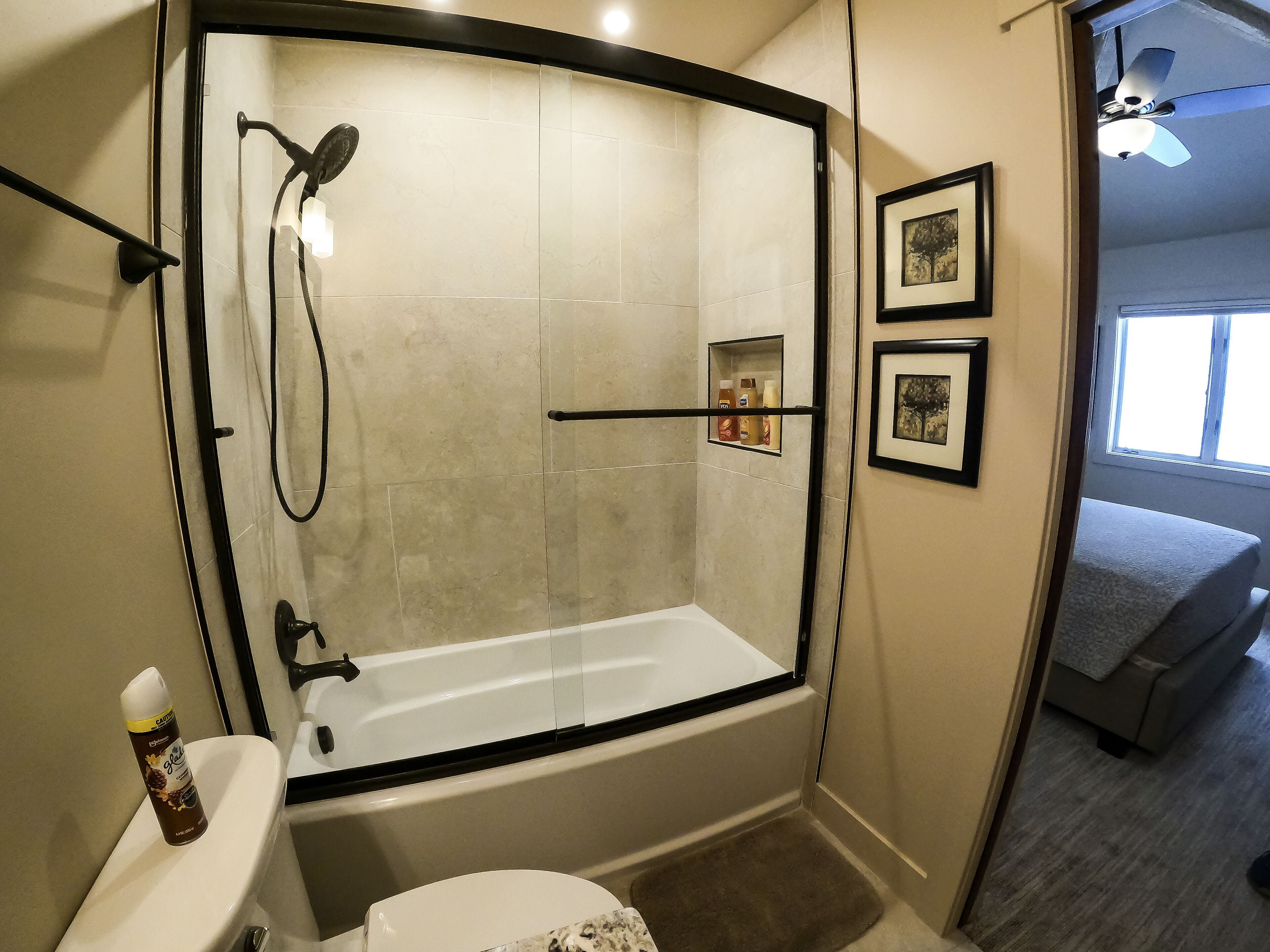 A modern bathroom with a glass-enclosed shower, a toilet, and a small shelf with toiletries.