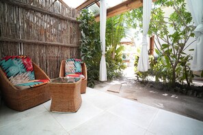 A wicker chair with a colorful cushion, a small table, and a bamboo fence in a patio area. - Olzadia Boutique Hotel (Michamvi)