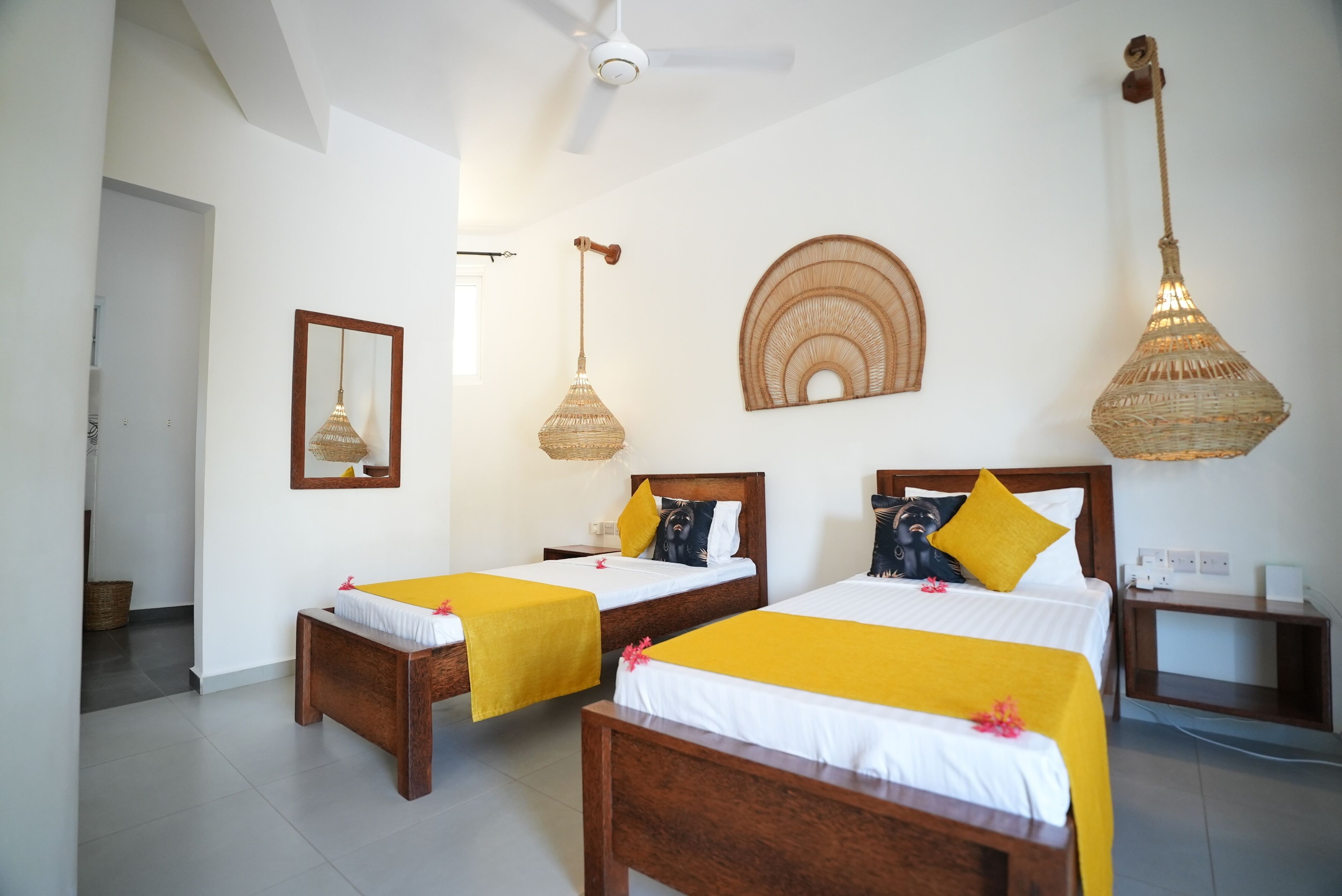 A hotel room with two wooden beds, a ceiling fan, a woven light fixture, and a wall-mounted mirror.