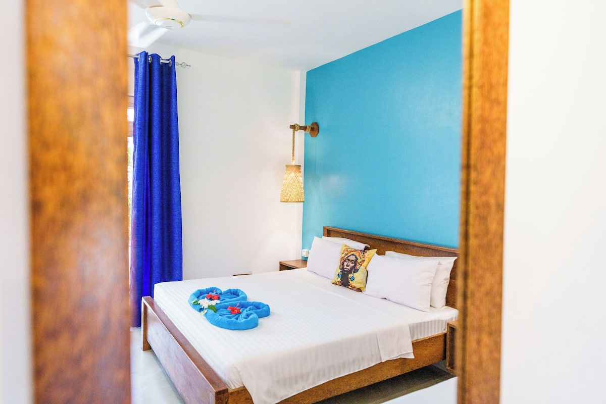 Ein Schlafzimmer mit einem Bett, einem Nachttisch, einer Wandlampe und einem blauen Vorhang.