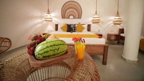 A room with a bed, a wooden side table with fruit and a drink, wicker furniture, and pendant lights. - Olzadia Boutique Hotel (Michamvi)