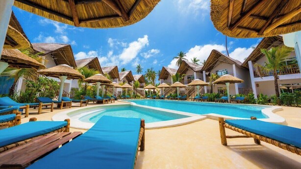 Ein Poolbereich eines Resorts mit Reetdachschirmen, Liegestühlen und blauem Himmel.