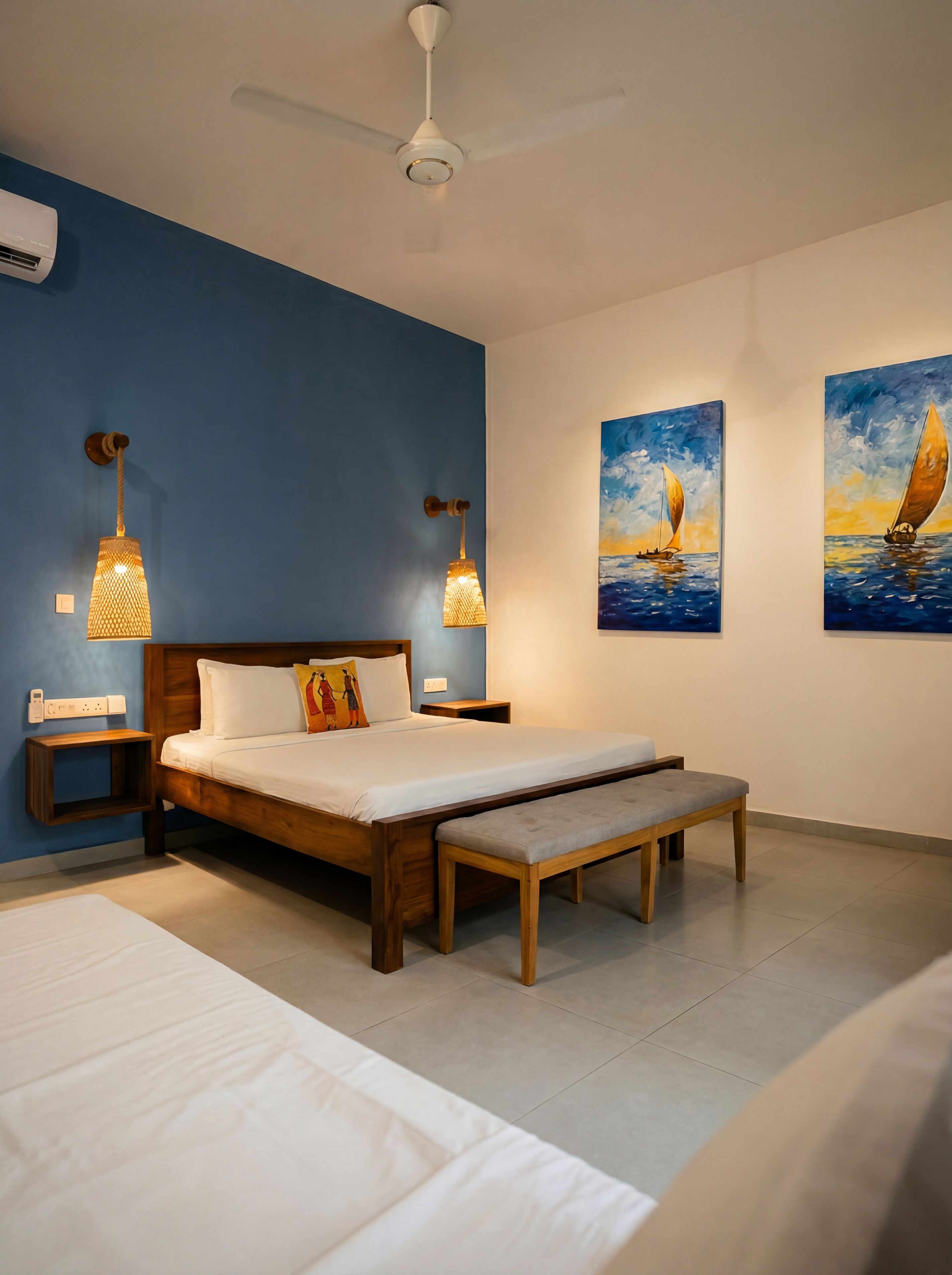 A bedroom with a bed, bedside tables, a bench, a ceiling fan, and wall art.
