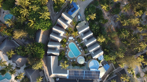 Eine Luftaufnahme eines Resorts mit mehreren Schwimmbecken, darunter ein großes, zentrales Becken, und einer Solaranlage.