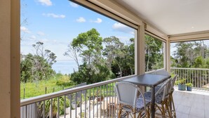 Un balcon avec une table et des chaises, donnant sur un paysage côtier avec des arbres et la mer.
