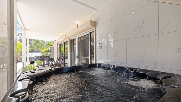 Un espace avec un jacuzzi entouré de parois en verre, une terrasse avec des meubles d’extérieur et une vue sur la verdure environnante.