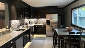 Een moderne keuken met donkere kastjes, roestvrijstalen apparatuur, een granieten aanrecht en een eethoek met een groot raam.
