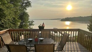 Een houten terras met een ronde tafel en stoelen, met uitzicht op een wateroppervlak en een verre kustlijn.