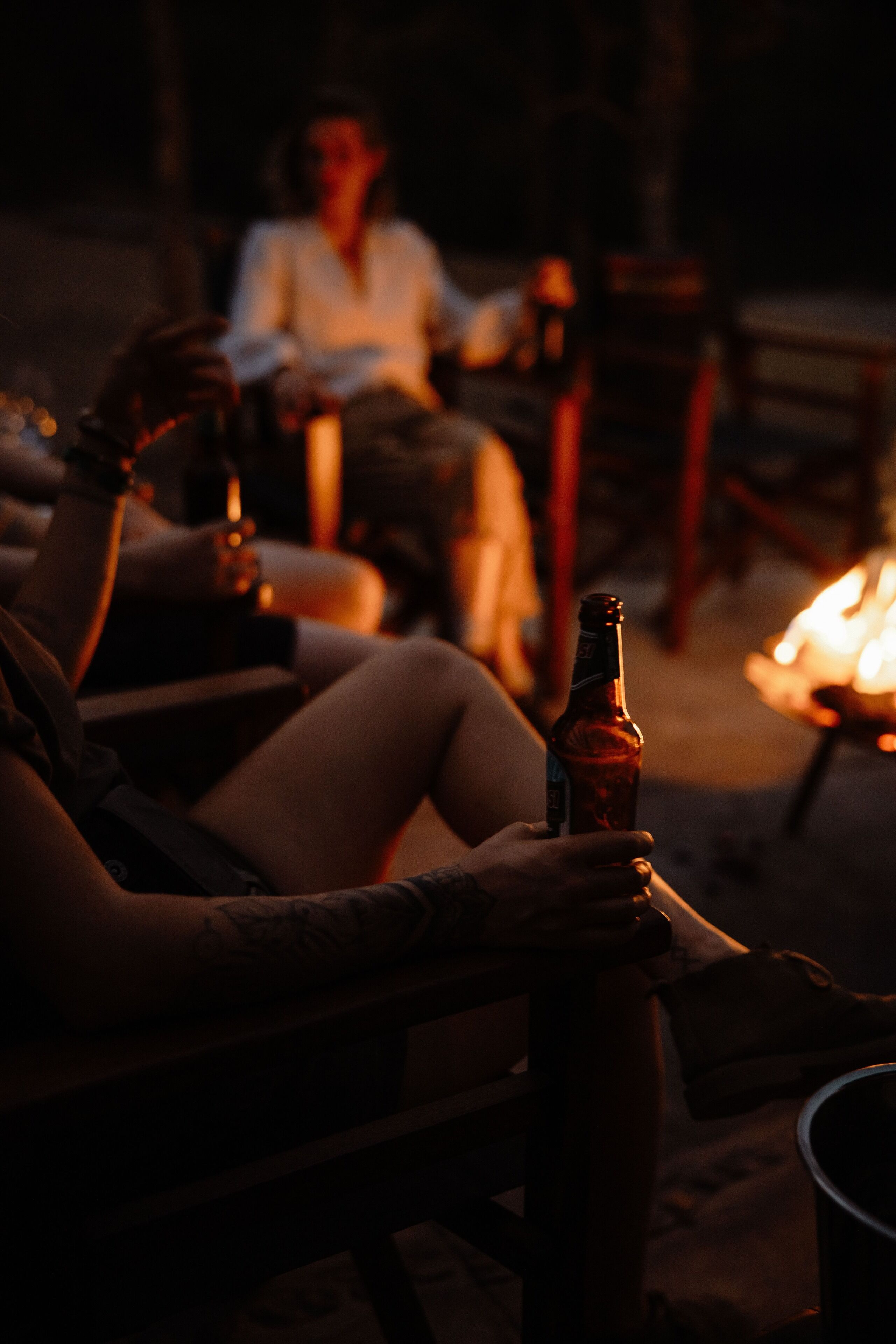 Una persona sentada junto al fuego sosteniendo una botella.