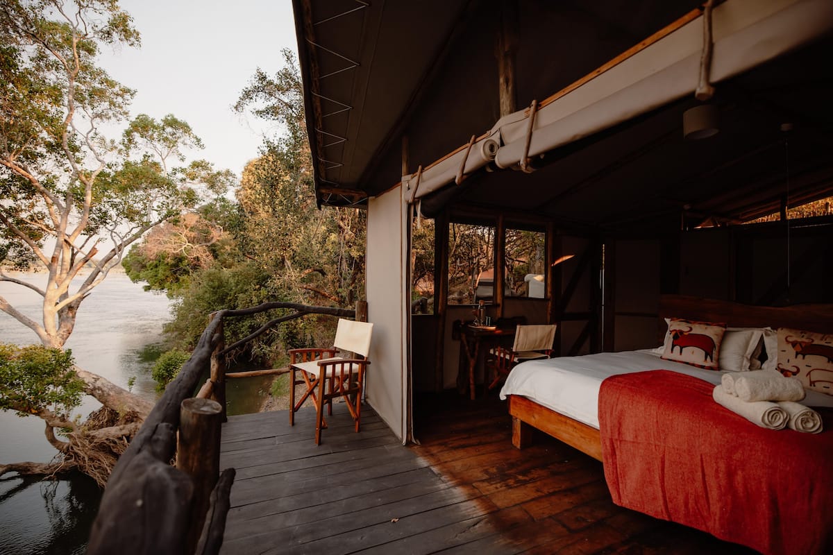 A wooden deck with a bed and chairs overlooking a body of water.