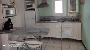Cocina compacta con microondas, estufa y pileta. Hay dos taburetes de bar y un refrigerador.