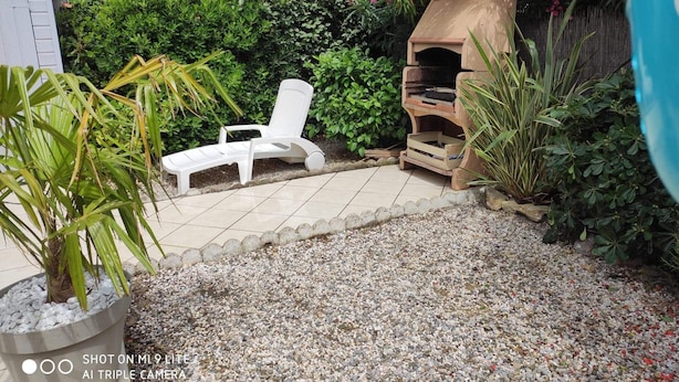 Un patio con una silla lounge blanca, una parrilla y una planta en maceta.