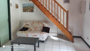 Una habitación con una escalera de madera, un sofá con tapicería floral, una mesita y una puerta con marco verde.