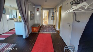 A hallway with a red carpet, a small table with a candle, and a coat rack. - Rotes Holzhaus am See (Nordingra)