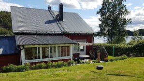 A house with a large window, a patio with outdoor furniture, and a view of a lake. - Rotes Holzhaus am See (Nordingra)