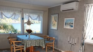 A dining area with a table set for four, surrounded by chairs, a patterned rug, and a view of a lake through large windows. - Rotes Holzhaus am See (Nordingra)