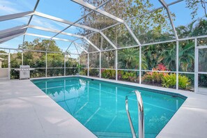 A swimming pool with a glass enclosure, surrounded by lush greenery and a barbecue area. - Live Like a Local: Charming Pool Home in Berkshire Lakes (Naples)