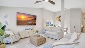 A modern living room with a large painting of a sunset, a white sofa, a coffee table, and a dining area with a white cabinet.