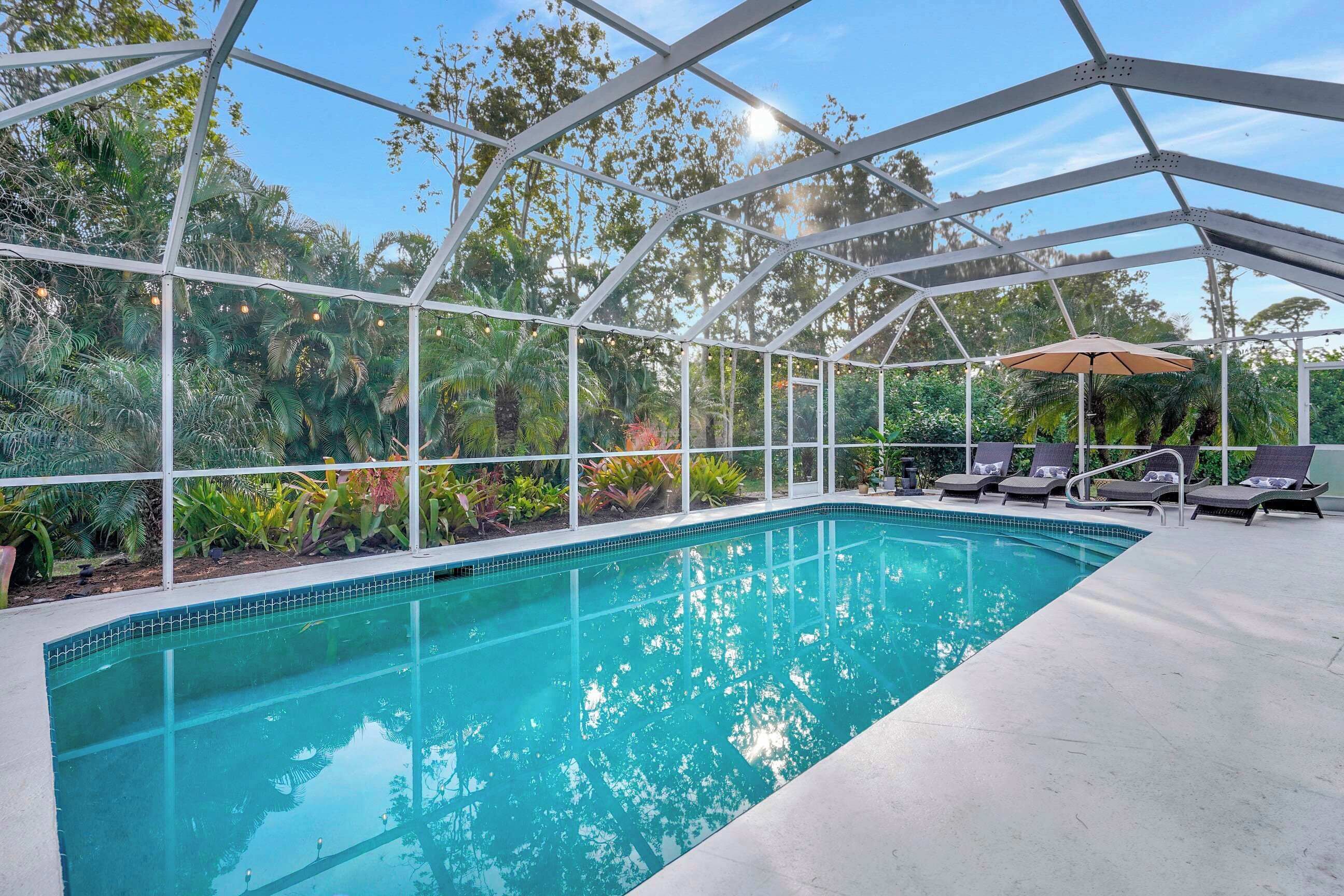 A pool area with a glass enclosure, lounge chairs, and a pergola with string lights.