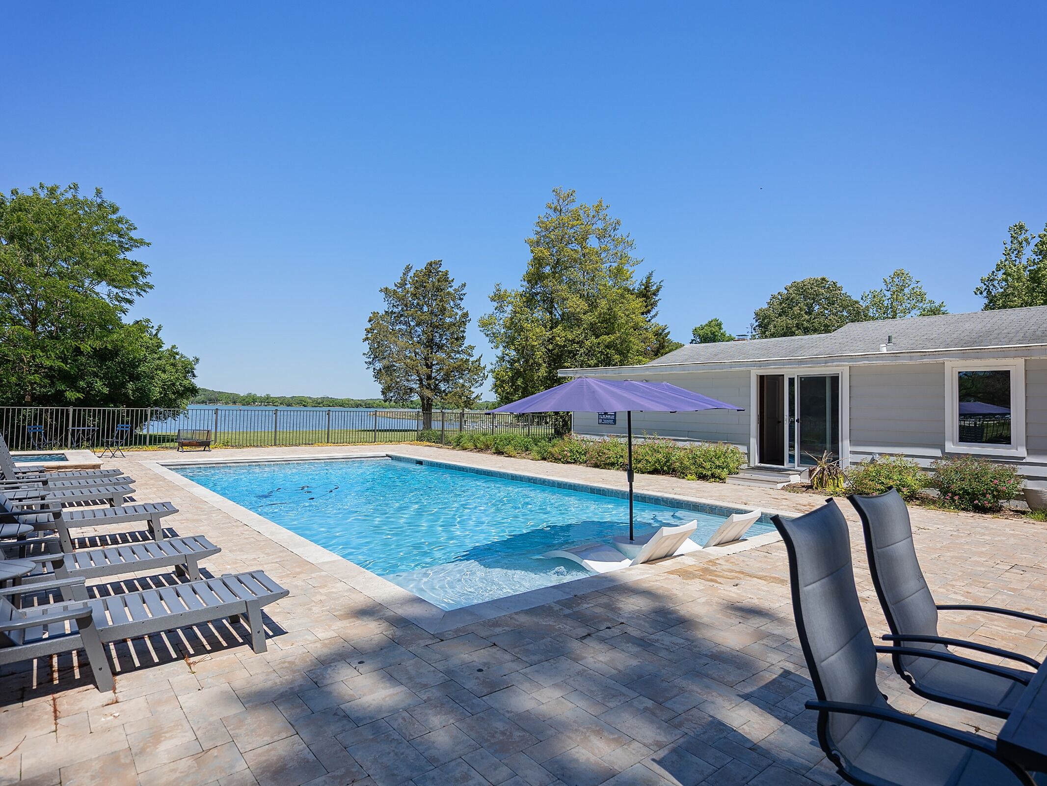 The property features a spacious pool deck with loungers and a lakefront setting, surrounded by mature trees and bordered by scenic water views.