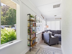 A living room with a bookshelf, a gray sofa, and a view of greenery outside. - Minutes from Downtown St. Michaels | Pool | Hot Tub (Bozman)