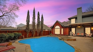 A backyard with a swimming pool, a wooden fence, and a brick house.