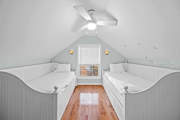 A bedroom with two single beds, a ceiling fan, and a window with blinds.