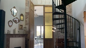A room with a spiral staircase, a fireplace, and a dining area visible through an open door. - Cosy Little House &garden (Arcachon)