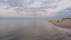 A beach with a pier extending into calm waters, a few people walking along the shore, and buildings in the background. - Cosy Little House &garden (Arcachon)