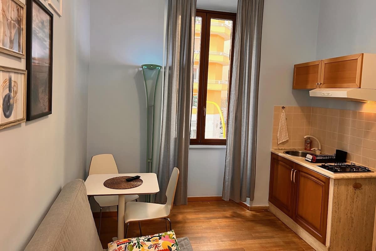 A compact kitchen with a dining area, a window with curtains, and a view of a building outside.