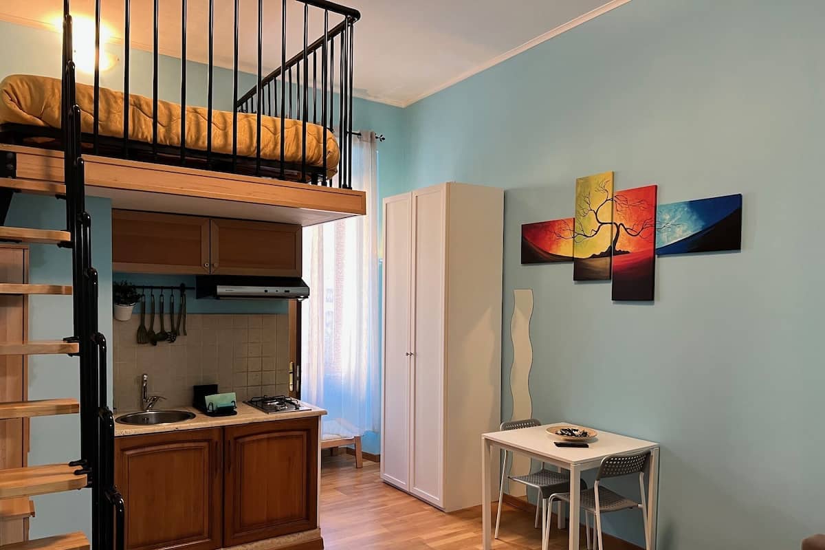 A compact apartment with a loft bedroom, kitchenette, dining area, and a single bed.
