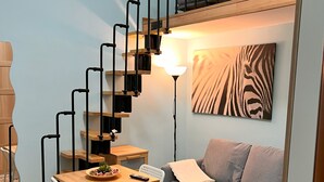 Ett kompakt bostadsutrymme med en trätrappa, en matplats med bord och stolar, en soffa och en väggdekoration med zebrasträck.