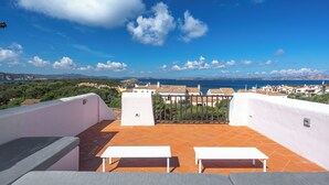 A terrace with white benches and a view of the sea and town.