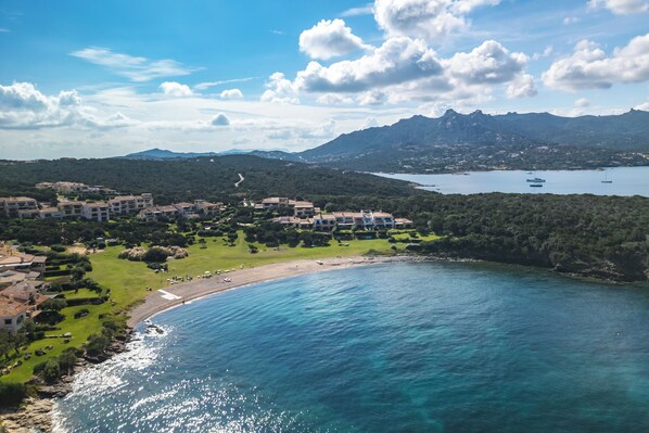 An aerial view of a coastal area with buildings, a beach, and a mountain range.