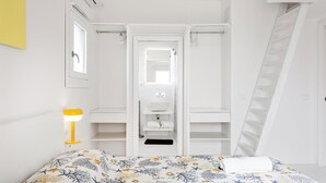 A bedroom with a bed, a bedside lamp, a wardrobe, and a bathroom with a sink and mirror.