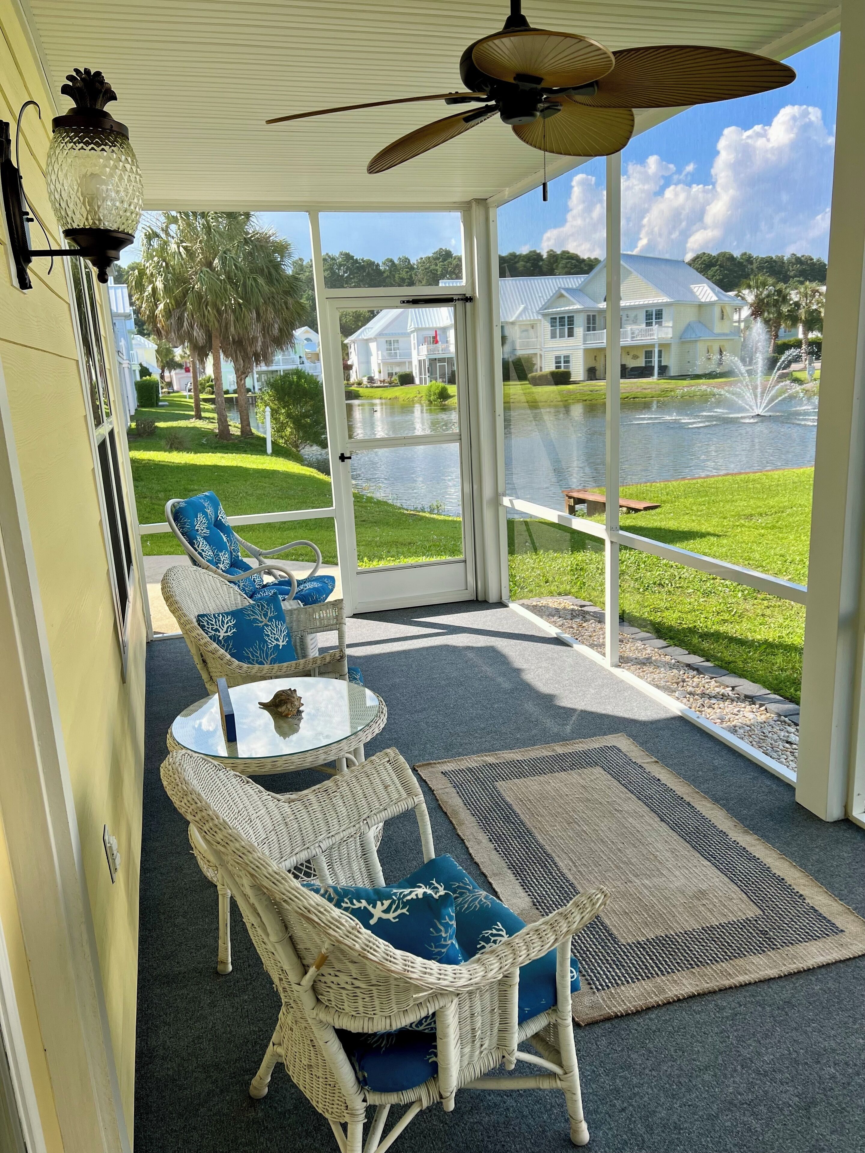 A covered patio with wicker furniture, a ceiling fan, and a view of a lake and houses.