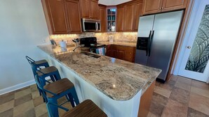 A kitchen with granite countertops, wooden cabinets, a stainless steel refrigerator, and a microwave. - 197 Georges Bay Road (Margonitaville) (Surfside Beach)
