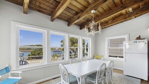 A dining area with a white table and chairs, large windows with a view of the beach, and a wooden ceiling. - Beach Nuts - Oceanfront, 4-bedrooms (Pawleys Island)