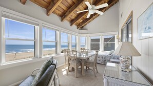 A room with a view of the beach, a ceiling fan, a dining table with chairs, a sofa, and a lamp. - Beach Nuts - Oceanfront, 4-bedrooms (Pawleys Island)