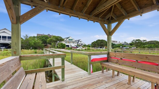 Une terrasse en bois avec des bancs, un espace abrité et une vue sur les maisons et la verdure.
