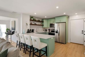 A modern kitchen with a central island, stainless steel appliances, and light green cabinetry. - Gorgeous Bayfront 2BR 3BA Condo l Marina Views (Panama City Beach)