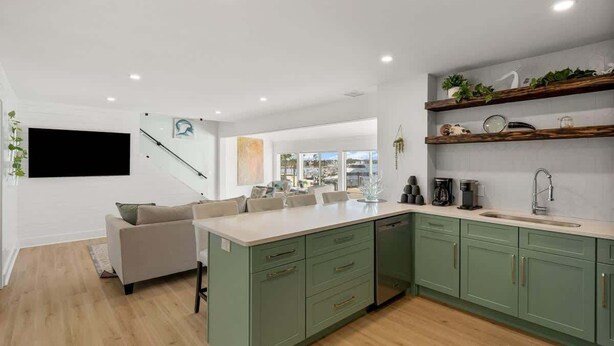 Una cocina moderna con armarios verdes, una isla central y un comedor con sofá.