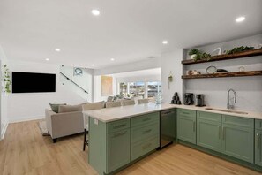 Uma cozinha moderna com armários verdes, uma ilha central e uma área de jantar com sofá.